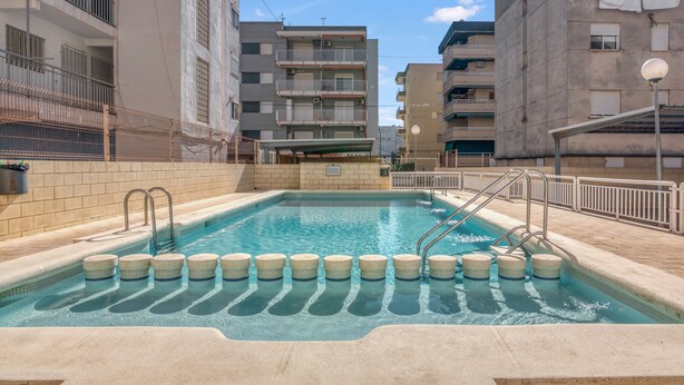 A swimming pool with steps, surrounded by multi-story buildings with balconies and railings. - Apartment 'On Daimús Beach' with Shared Pool, Wi-Fi and Air Conditioning (Daimús)