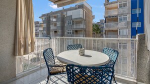 A balcony with a round table and chairs, a view of multi-story buildings, and a clear sky. - Apartment 'On Daimús Beach' with Shared Pool, Wi-Fi and Air Conditioning (Daimús)