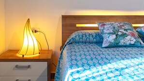 Una cama bien tendida con ropa de cama azul y blanca estampada, una lámpara de noche y una mesita de noche de madera con cajones.