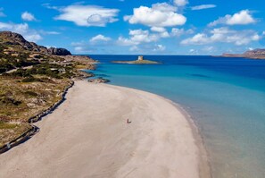 Eine Küstenlandschaft mit Sandstrand, einem kleinen Turm und klarem, blauem Wasser.