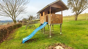 Une cabane en bois avec un toboggan, installée dans un espace herbeux.