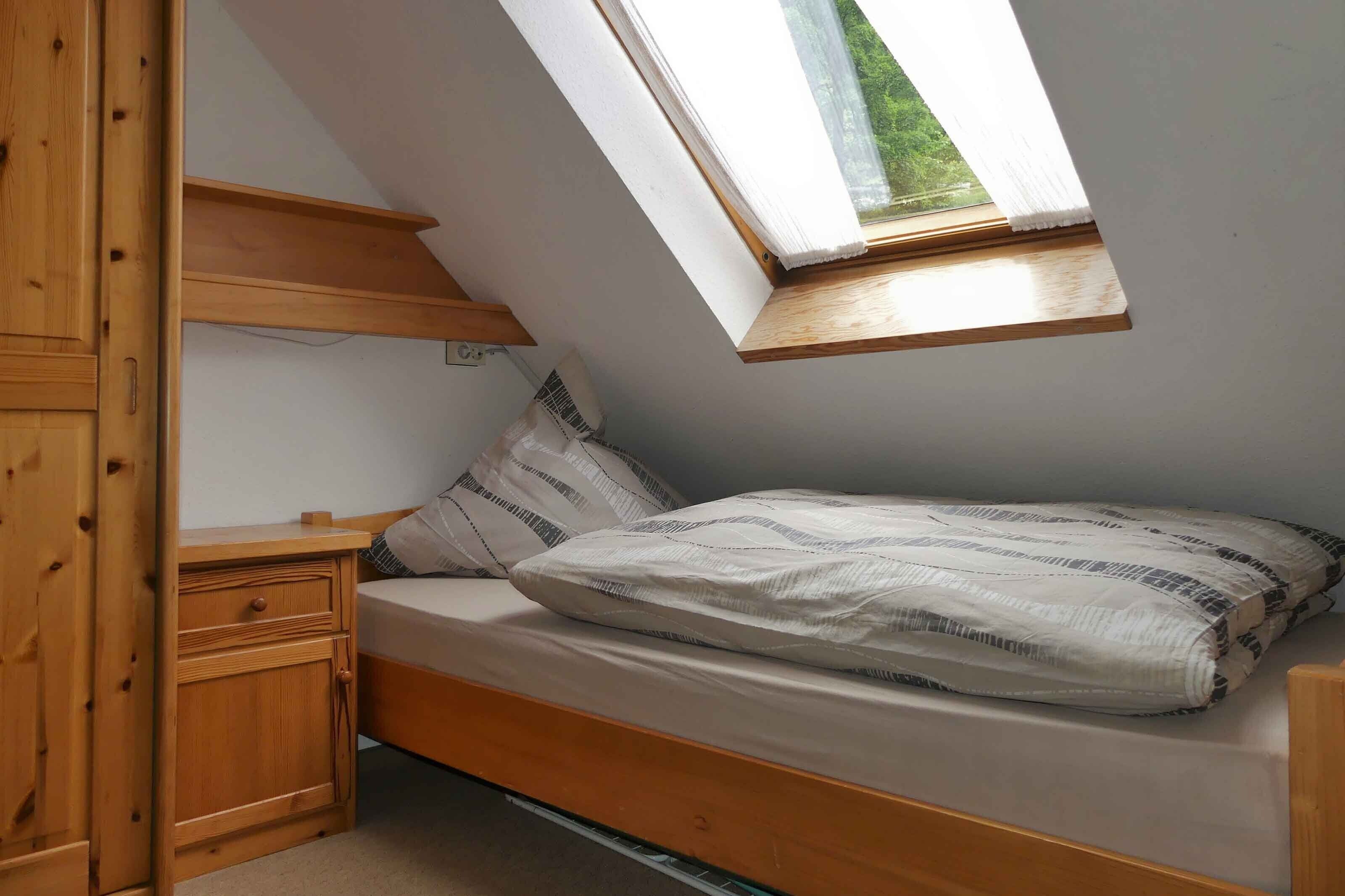 Un dormitorio con techo inclinado, tragaluz, estructura de cama de madera y mesita de noche.