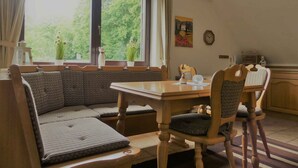 Un comedor con mesa y sillas de madera, un banco y una ventana con vista a follaje.