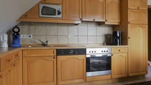 Una cocina con armarios de madera, microondas, cafetera, lavavajillas y horno.