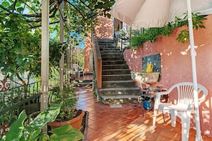 A patio area with a tiled floor, a staircase, potted plants, a white plastic chair, and a grill.