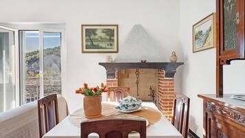 Un coin repas avec une table dressée pour deux personnes, une cheminée et une vue par la fenêtre.