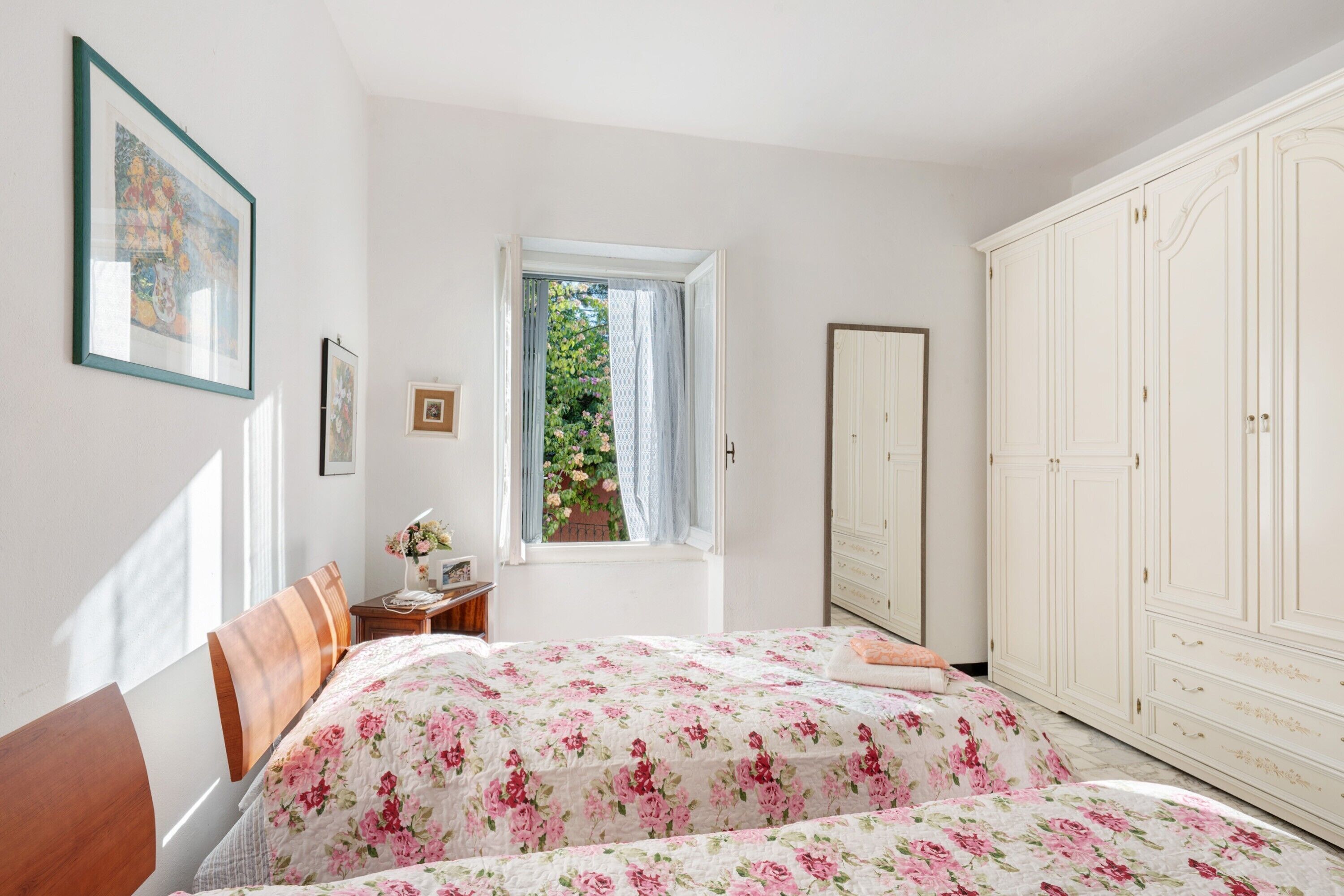 A bedroom with a bed, a window with curtains, a wardrobe, and a framed picture on the wall.