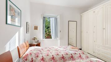 A bedroom with a bed, a window with curtains, a wardrobe, and a framed picture on the wall.