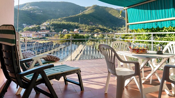 Een balkon met uitzicht op groene heuvels, een tafel met stoelen en een gestreepte stoel.