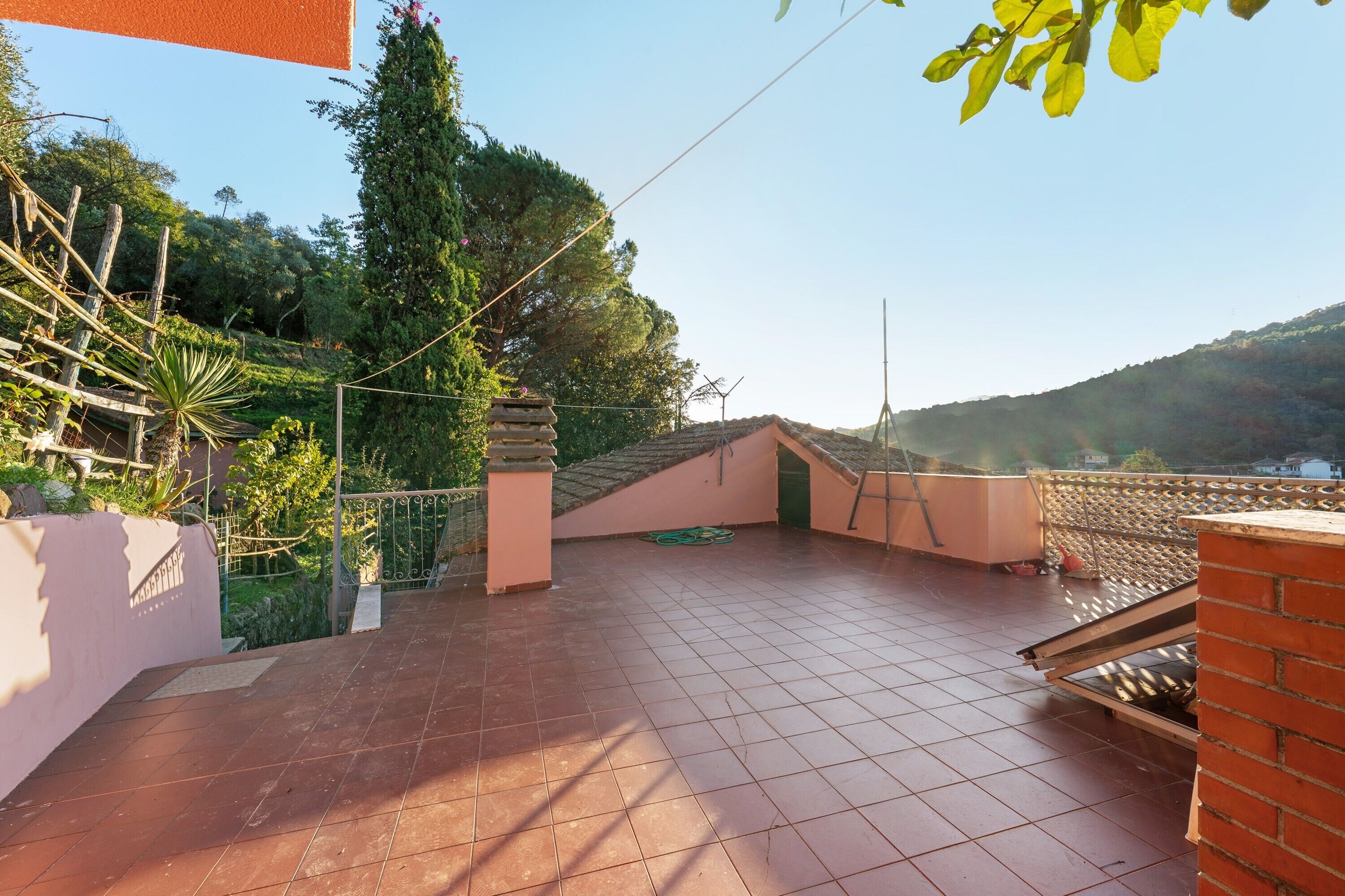 Una terrazza sul tetto con pavimento piastrellato, un muro in mattoni e vista su un paesaggio collinare.