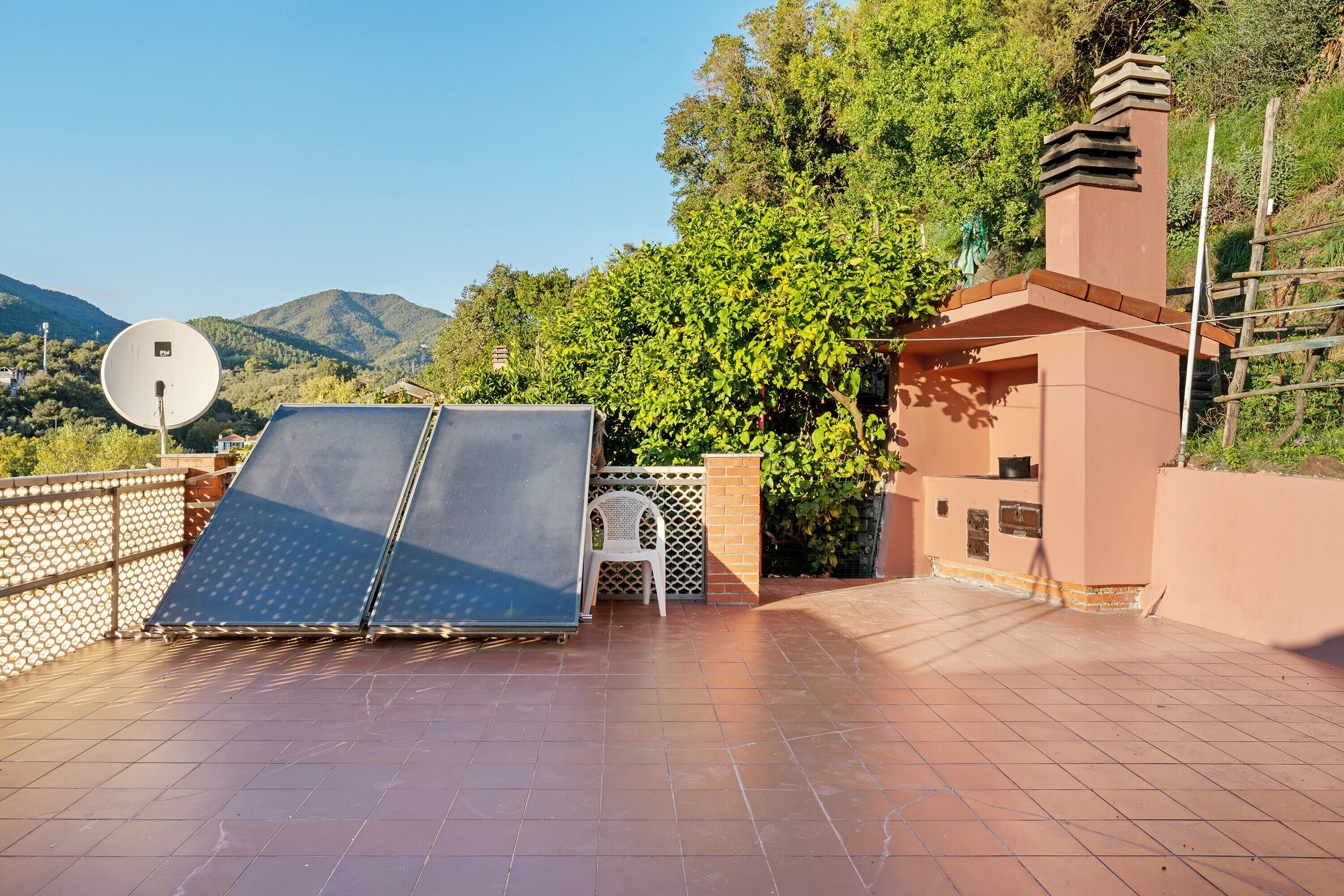 A rooftop terrace with solar panels, a satellite dish, and a view of mountains.
