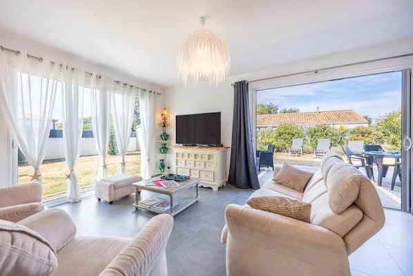 A modern living room with a flat-screen TV, beige sofas, a coffee table, and a view of the outdoors.