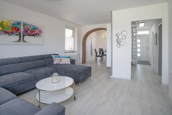 A modern living room with a grey sectional sofa, a white coffee table, and a dining area with a table and chairs.
