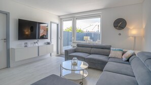 Una sala de estar moderna con un sofá gris, una mesa de centro de cristal, un televisor de pantalla plana y un ventanal grande.