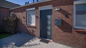 Un edificio de ladrillo con una puerta oscura, una ventana y un pequeño espacio exterior con una jardinera.