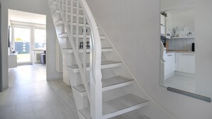 Una escalera moderna con barandillas blancas y una zona de cocina con armarios blancos y encimera.
