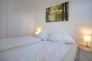 A bedroom with two beds, a wardrobe, a painting, and bedside lamps.