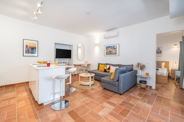 Un espace de vie moderne comprenant un coin cuisine, un canapé gris et une table à manger.