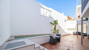 Una terraza en la azotea con una piscina pequeña, mobiliario exterior y una escalera que sube a un nivel superior.