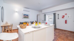 Una cocina moderna con una isla central, una zona de comedor con sillas, una mesa blanca y vistas al exterior.