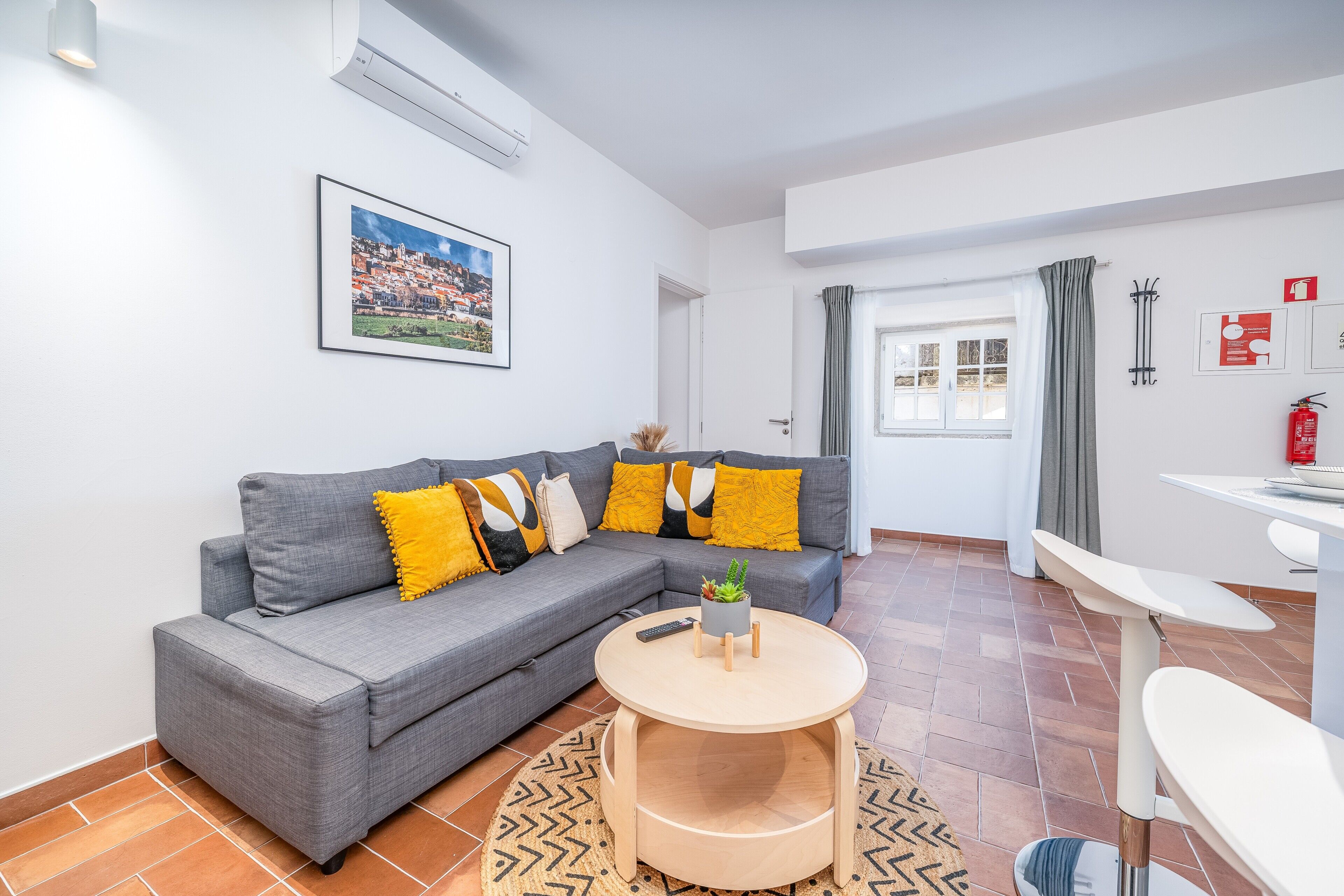 A modern living room with a grey sectional sofa, a round wooden coffee table, and a cityscape painting on the wall.