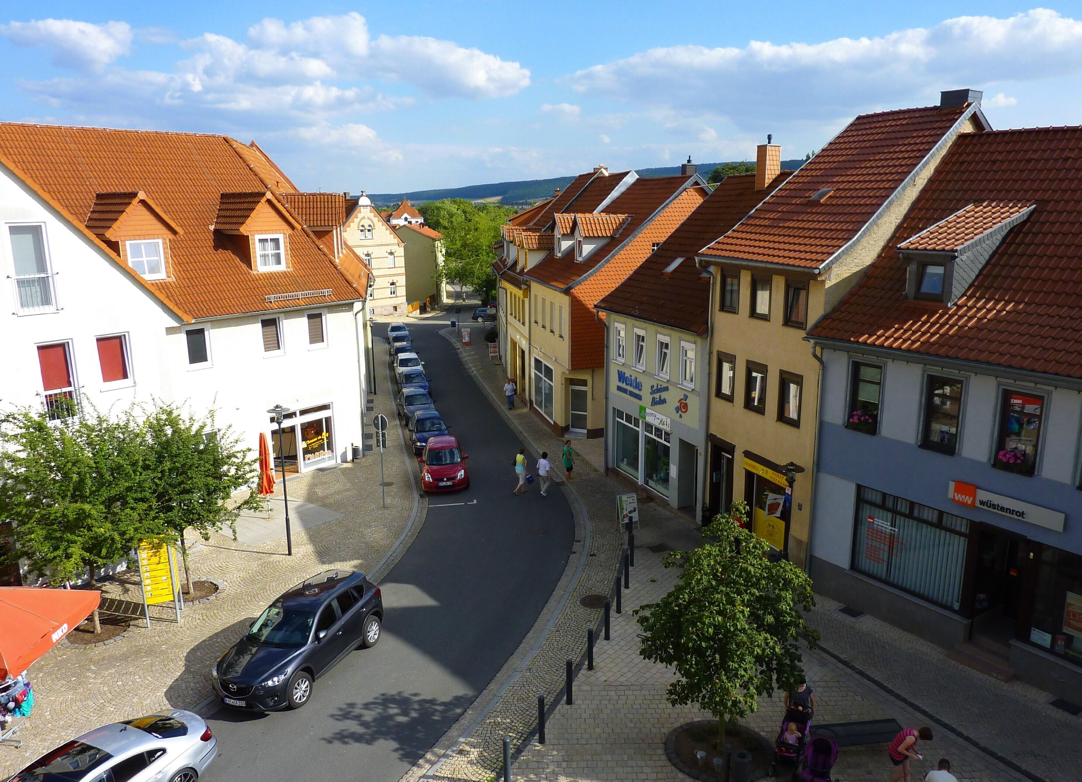 Straßenansicht mit traditioneller europäischer Architektur, eine Reihe geparkter Autos und Fußgänger.