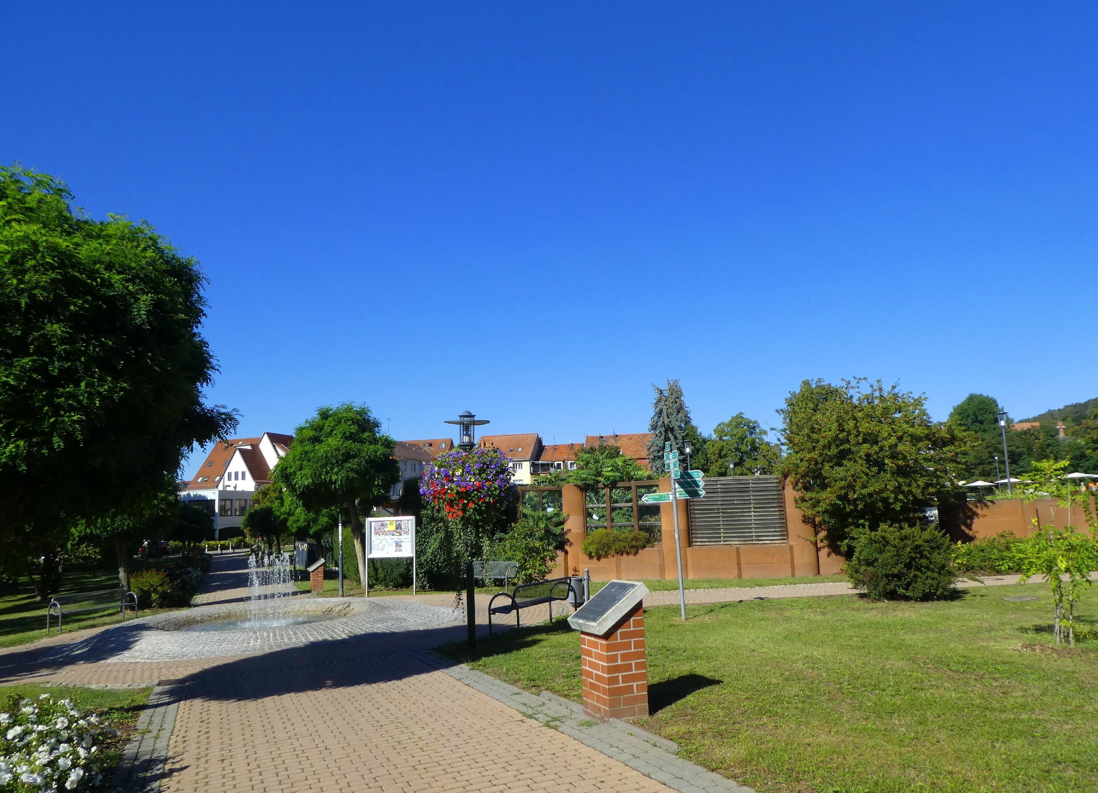 Ein Park mit einem Brunnen, einem Wegweiser und einer Backsteinmauer.