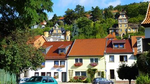 Une rangée de bâtiments de style européen traditionnel, avec des toits recouverts de tuiles rouges, dont certains sont ornés de jardinières, et une rue au premier plan.