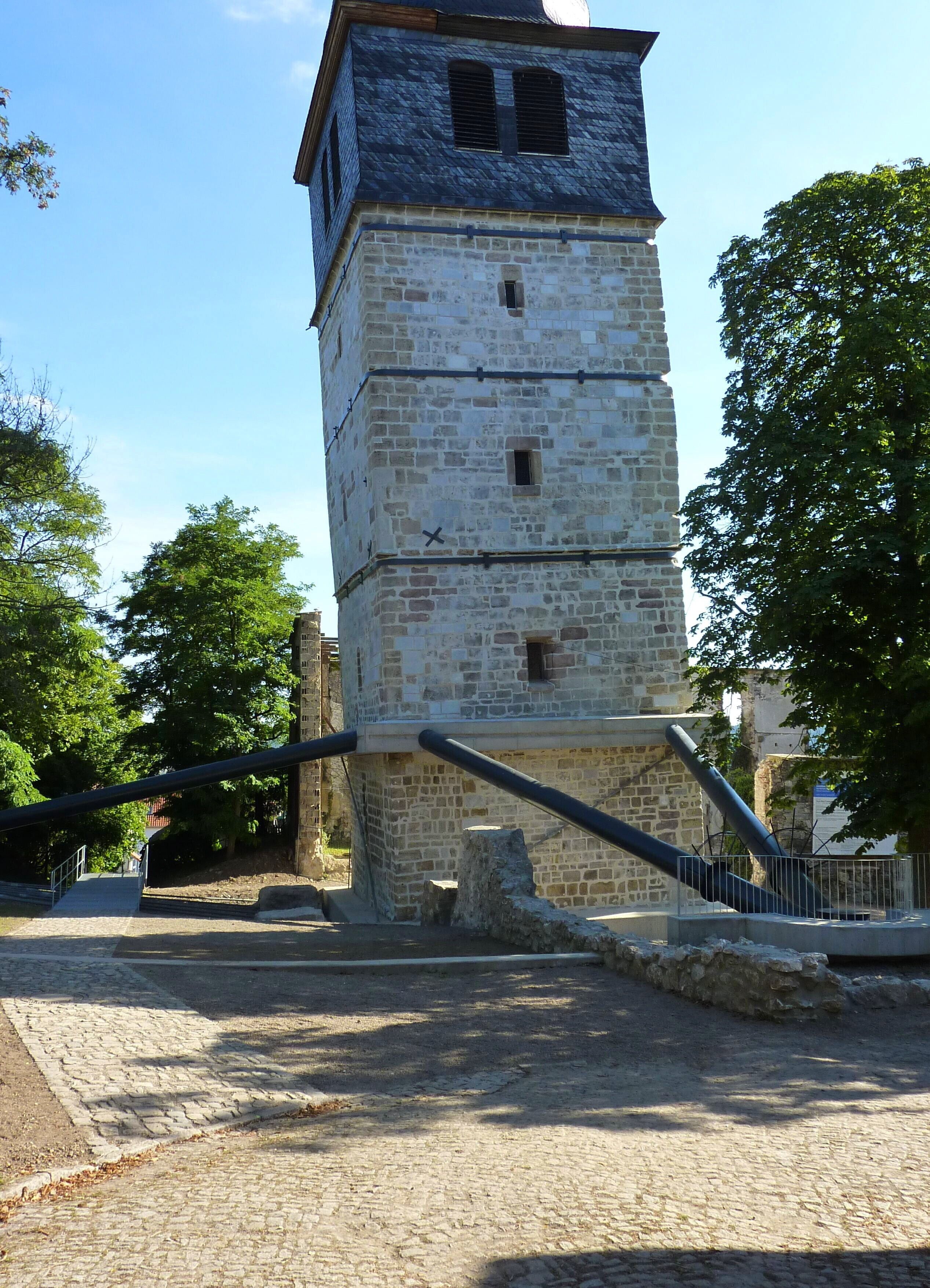 A stone tower with a staircase leading up to it, surrounded by trees and a paved area.