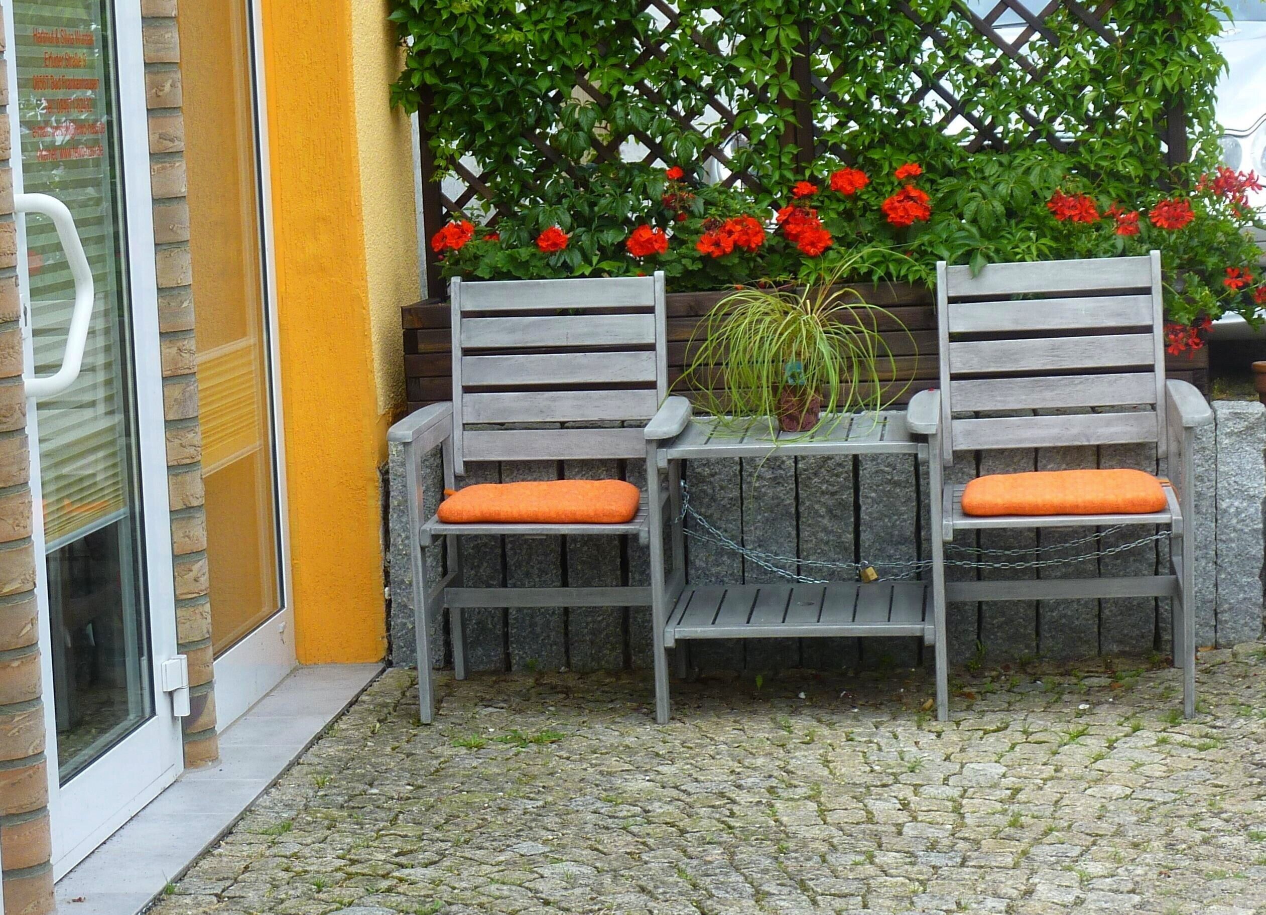 Two wooden chairs with orange cushions, a small table, and a potted plant.