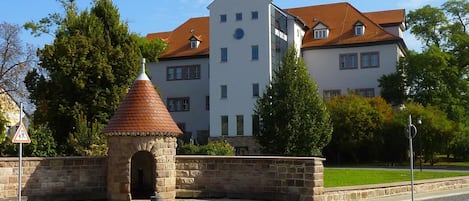 Une structure en pierre surmontée d’un toit conique, avec des bancs et, au fond, un bâtiment doté d’un clocher.
