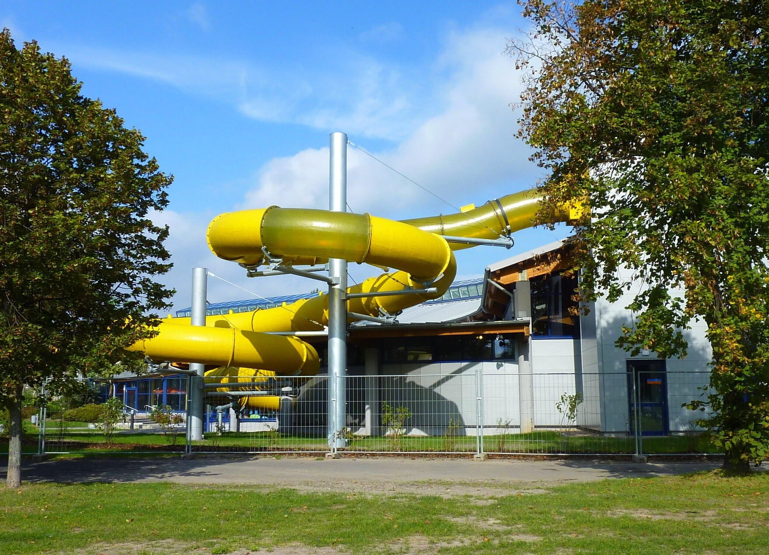 A building with a unique yellow structure, possibly a water feature, in front of it.