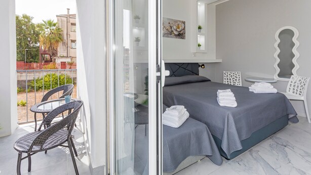 Een hotelkamer met balkon, een bed met netjes opgevouwen handdoeken en een zithoek met stoelen.