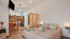 Ein Schlafzimmer mit Bett, Fernseher, einer Holztrennung und einer Küche im Hintergrund.