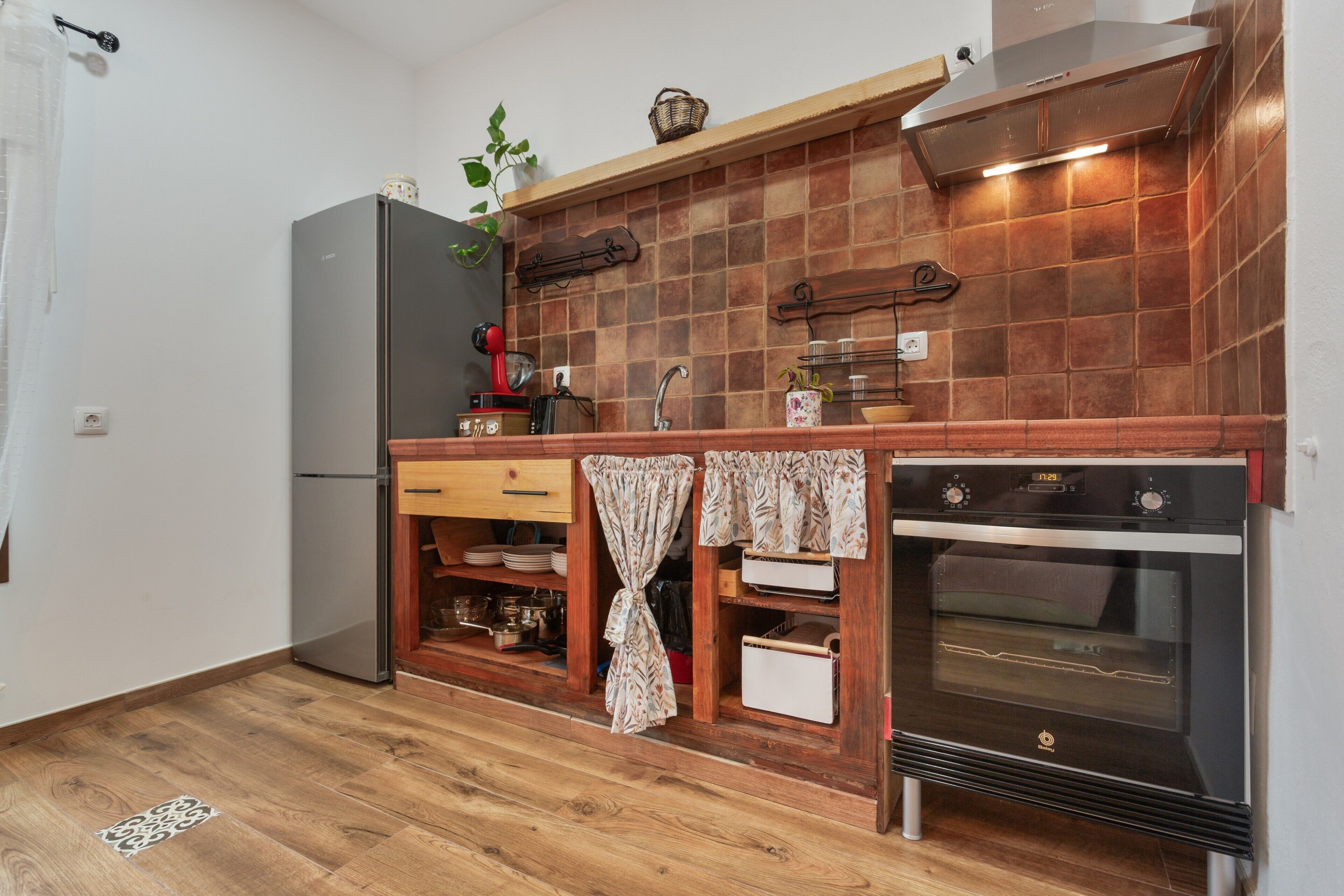 A compact kitchen with a refrigerator, oven, wooden cabinets, and a tiled backsplash.