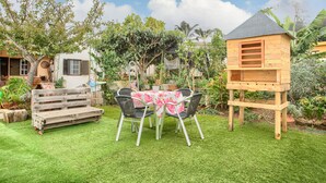Eine Terrasse mit einer Holzbank, einem Tisch mit Stühlen und einem hölzernen Spielhäuschen.