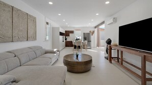Una sala de estar moderna con un sofá, una mesa redonda de centro y un televisor de pantalla plana sobre un soporte de madera.