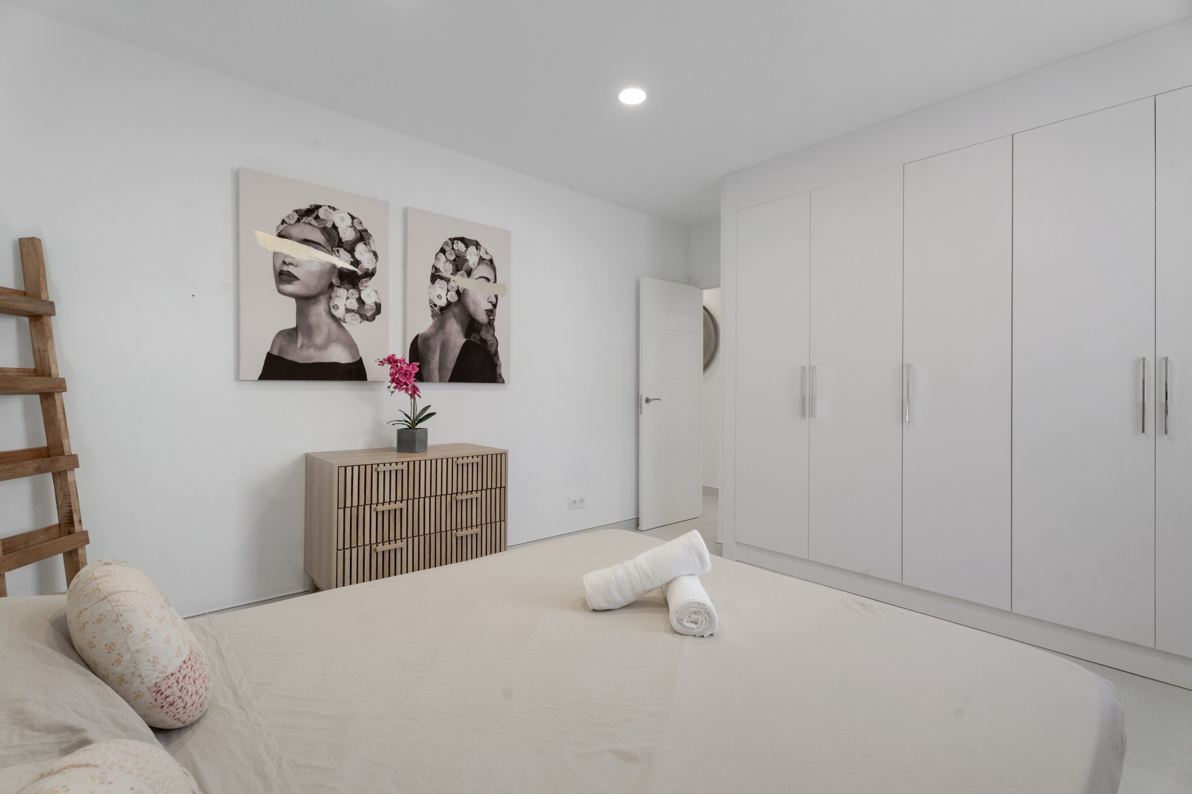A bedroom with a bed, a wooden ladder, a cabinet, and two wall-mounted artworks.