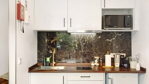 A kitchen with white cabinets, a marble backsplash, a microwave, a coffee maker, and a sink.