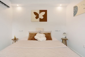 A bedroom with a bed, two wall-mounted butterfly art pieces, a bedside table with a lamp, and a wall socket.