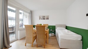 Quarto com cama, mesa de jantar com cadeiras, uma mesinha lateral e vista para o exterior.