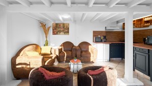 Ein Wohnzimmer mit einer Sofagarnitur, einem Couchtisch und einer Küchenzeile mit Schränken und Geräten.