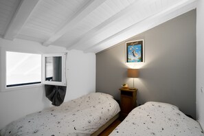 Un dormitorio con dos camas, una ventana, una lámpara de pared y un cuadro enmarcado.