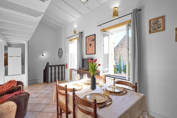 A dining area with a table set for four, a vase with flowers, and a view of the outside.