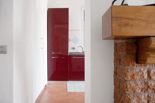 A kitchen with red cabinets, a stone wall, and a white door leading to another room. - Apartment 'Mora' with Mountain View, Private Terrace and Wi-Fi (Cantello)