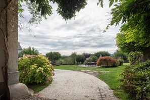 Ein Pflasterweg schlängelt sich durch einen Garten mit verschiedenen Pflanzen und Bäumen.
