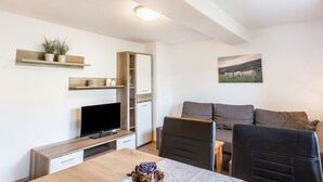 A modern living room with a TV, sofa, dining table, and decorative items. - Apartment 'Pusteblume' with shared terrace and Wi-Fi (Schmallenberg)