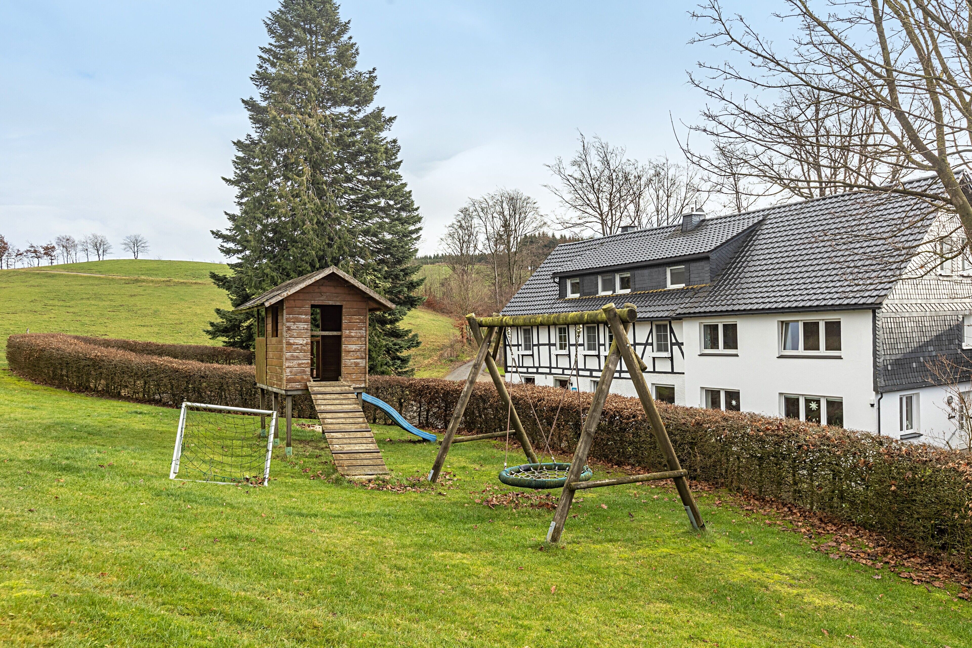Een woonhuis met een groot huis, een houten speelhuisje en een schommel.