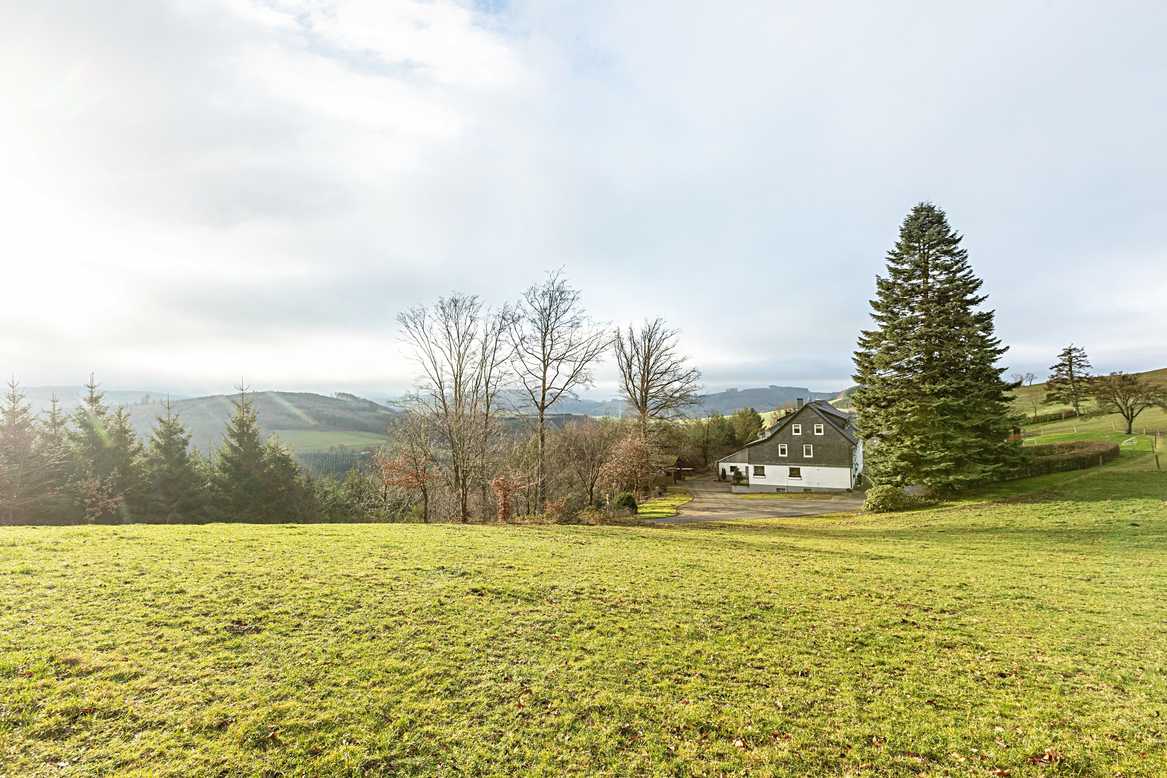 A house with a large lawn, a driveway, and a view of distant hills.
