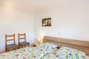 Une chambre à coucher avec deux chaises en bois, une table de chevet avec une lampe et un lit avec une literie à motifs floraux.